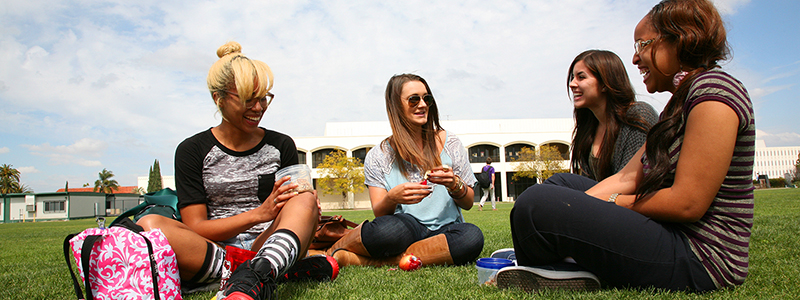 4 female students sitting on grass on campus eating lunch