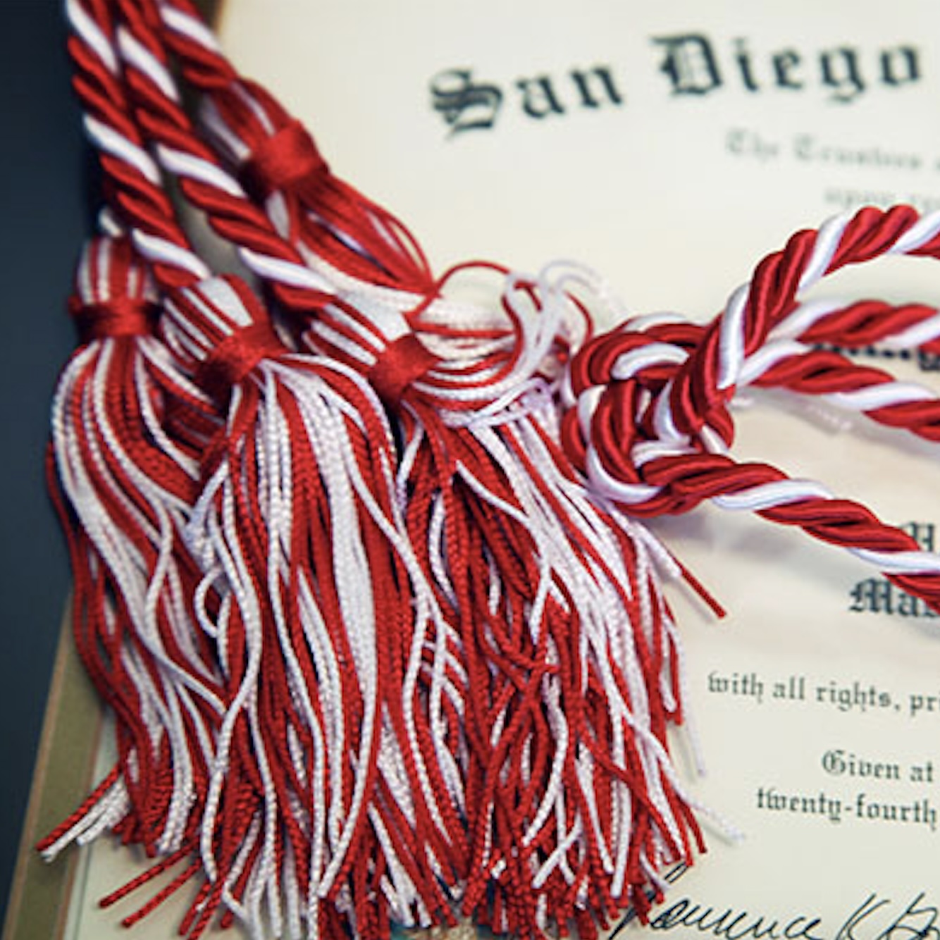 SDSU diploma in the background with a red and white legacy cord on top of it.