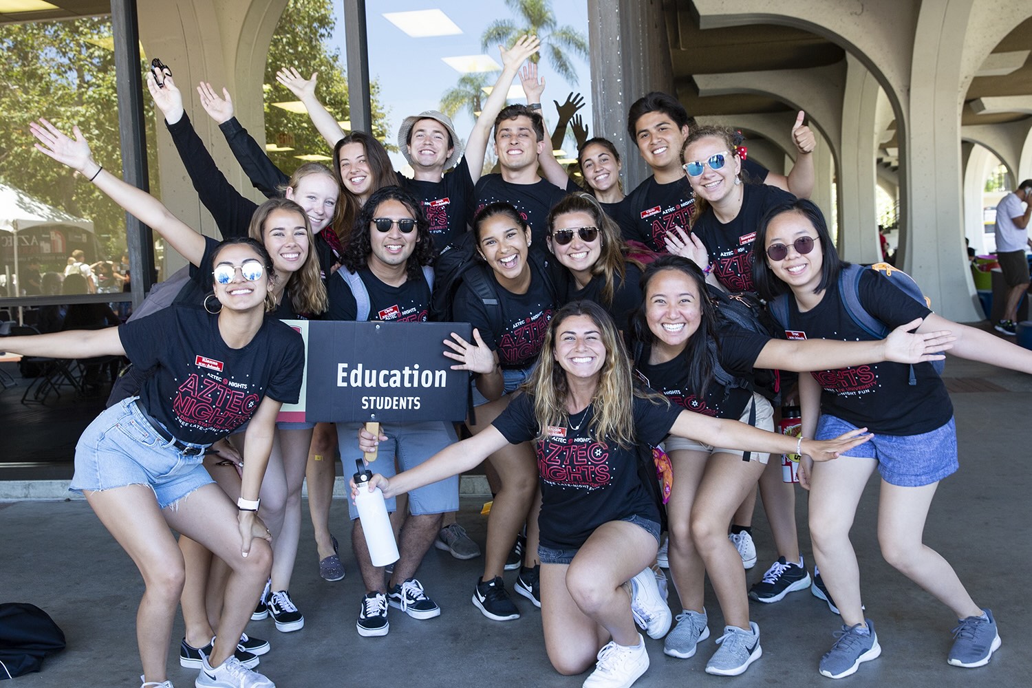 group of orientation staff in black orientation shirts and shorts, holding hands out and smiling